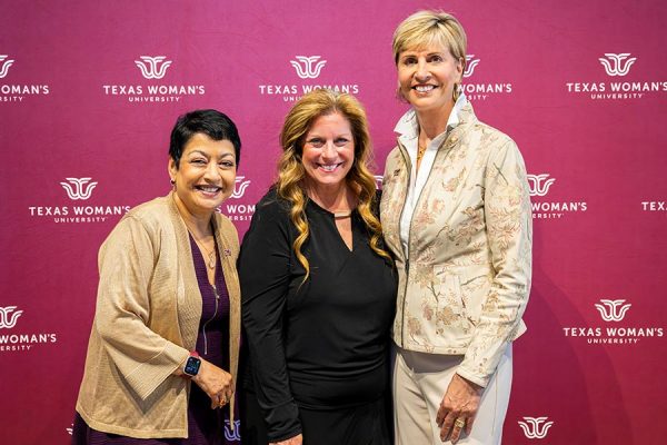 3 women stand smiling in from of a maroon backdrop