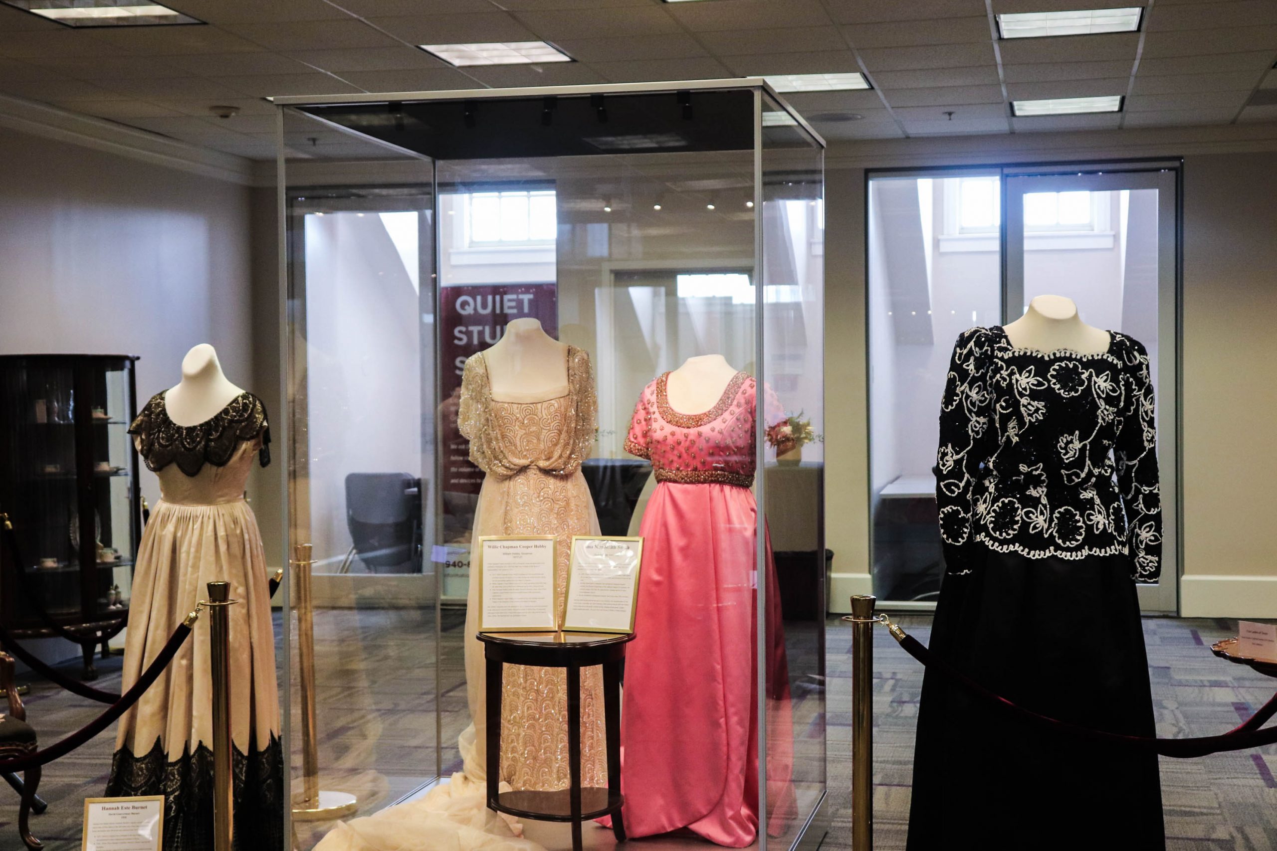 Dresses on forms sit in and outside of glasses cases in library