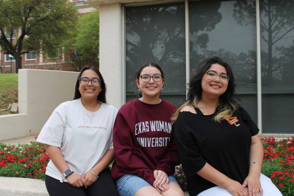 Three girls site next to each other in front of flowerbed